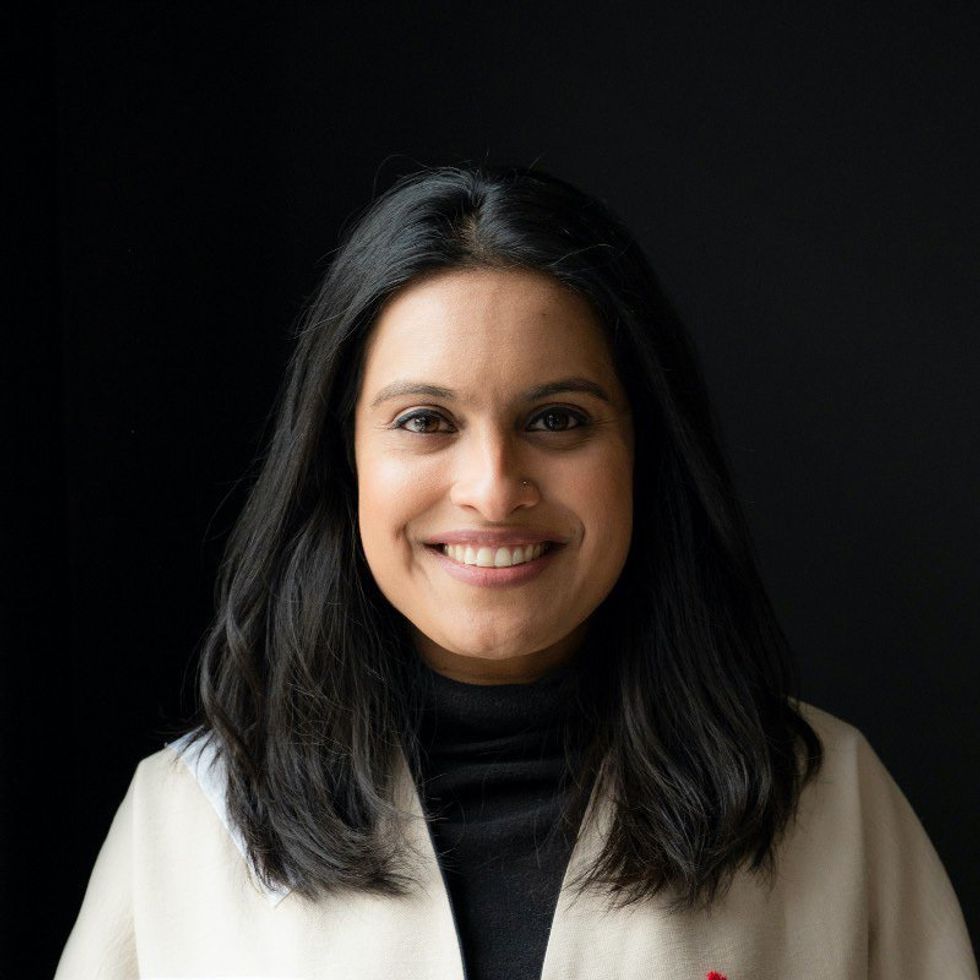 portrait of a woman in a white coat smiling for the camera against a black background