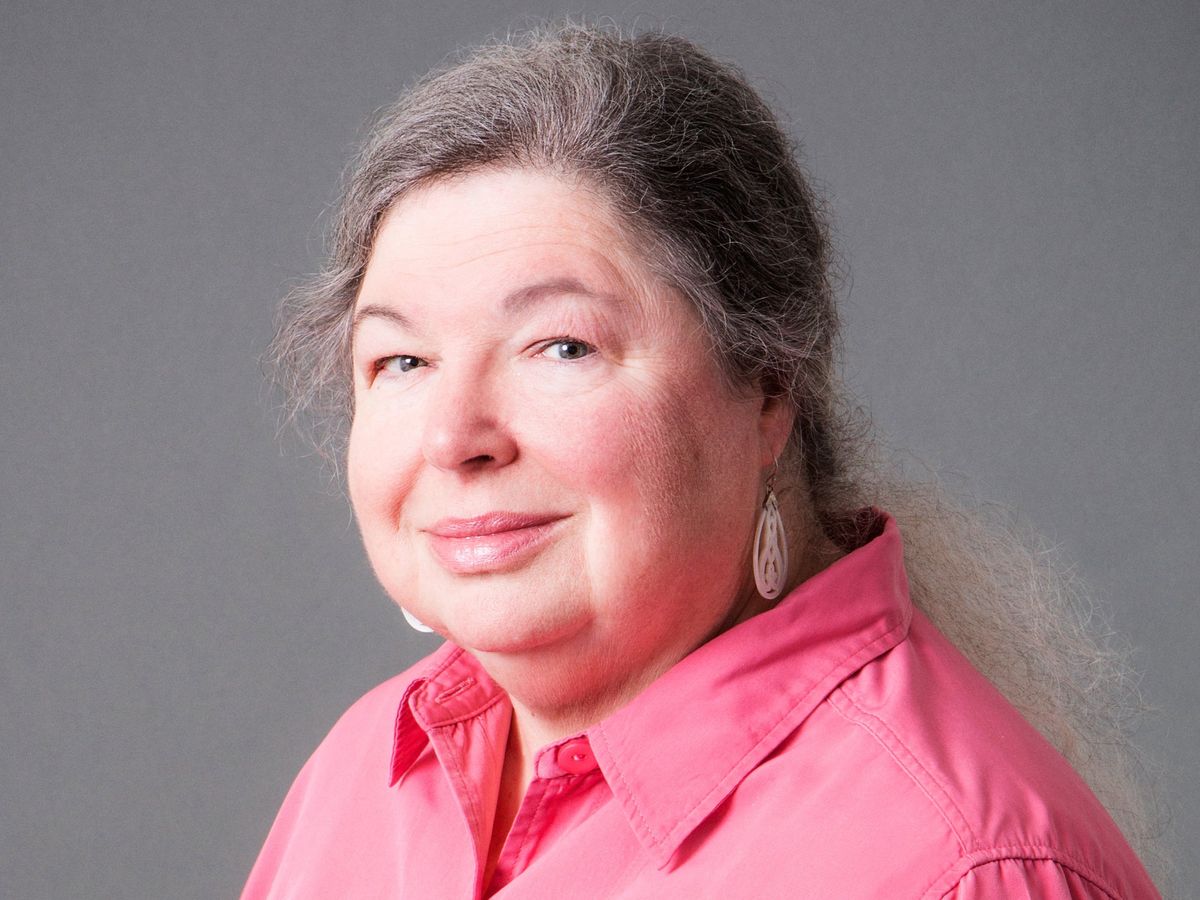 portrait of a woman wearing a bright pink shirt against a gray background