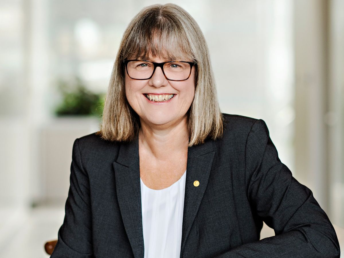 portrait of woman wearing glasses and suit jacket smiling at camera against at white background