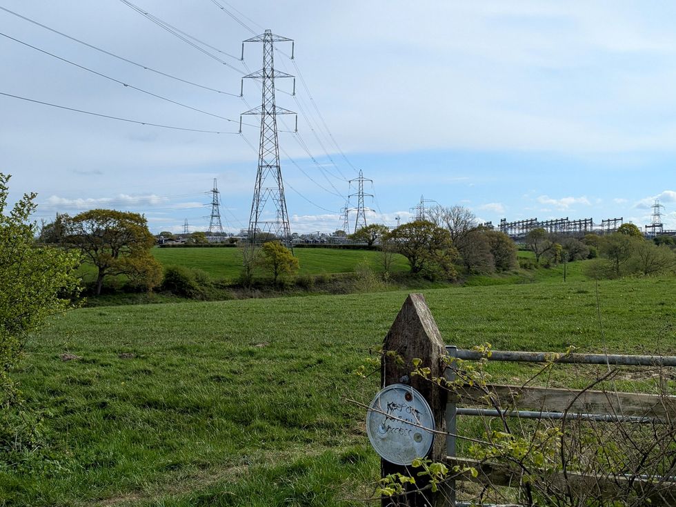 Power lines crossing a rural pasture, with an old fence in the foreground and a substation in the background.