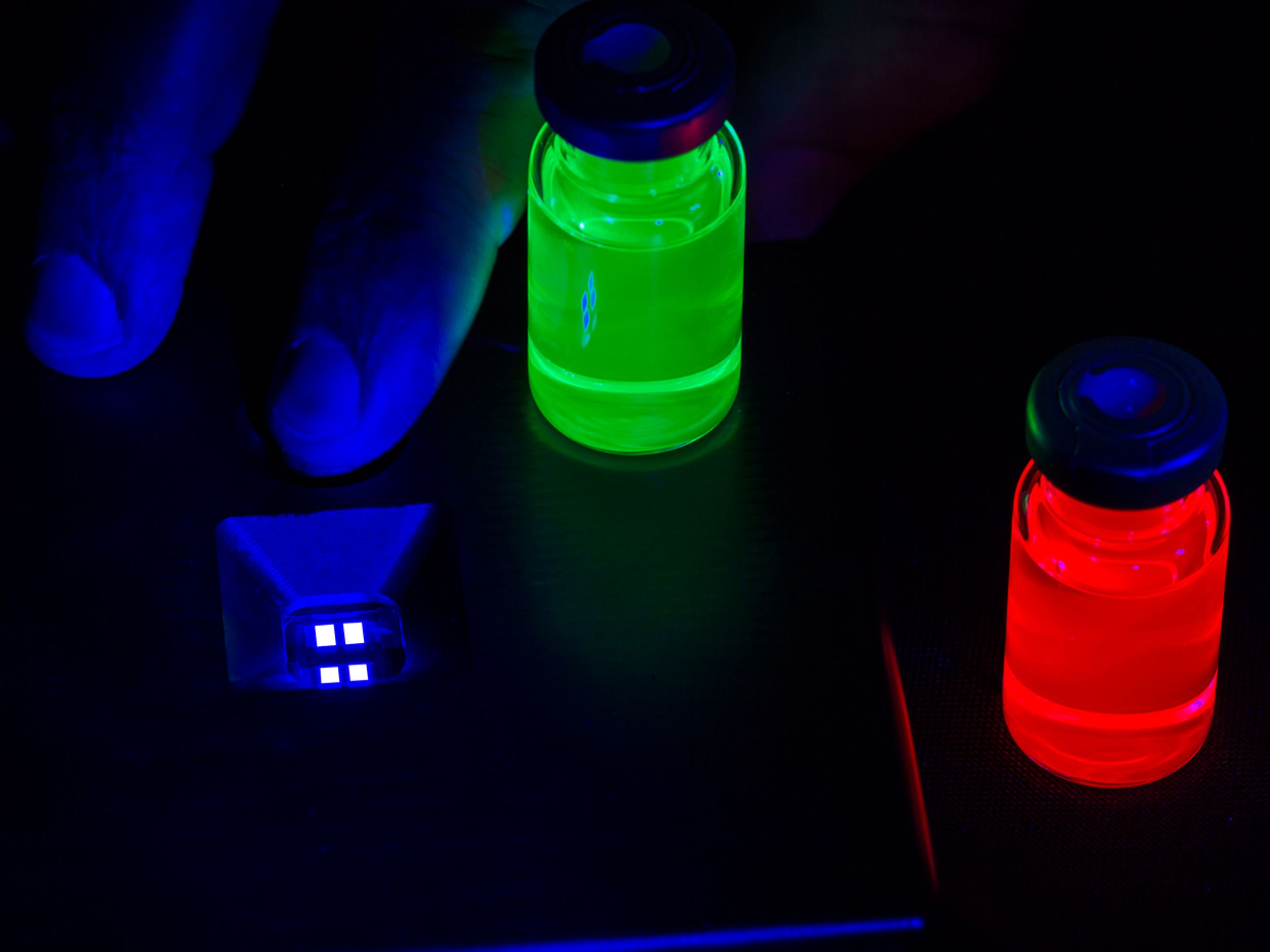 Printed pixels of electroluminescent blue quantum dots alongside vials of red and green quantum dots.  