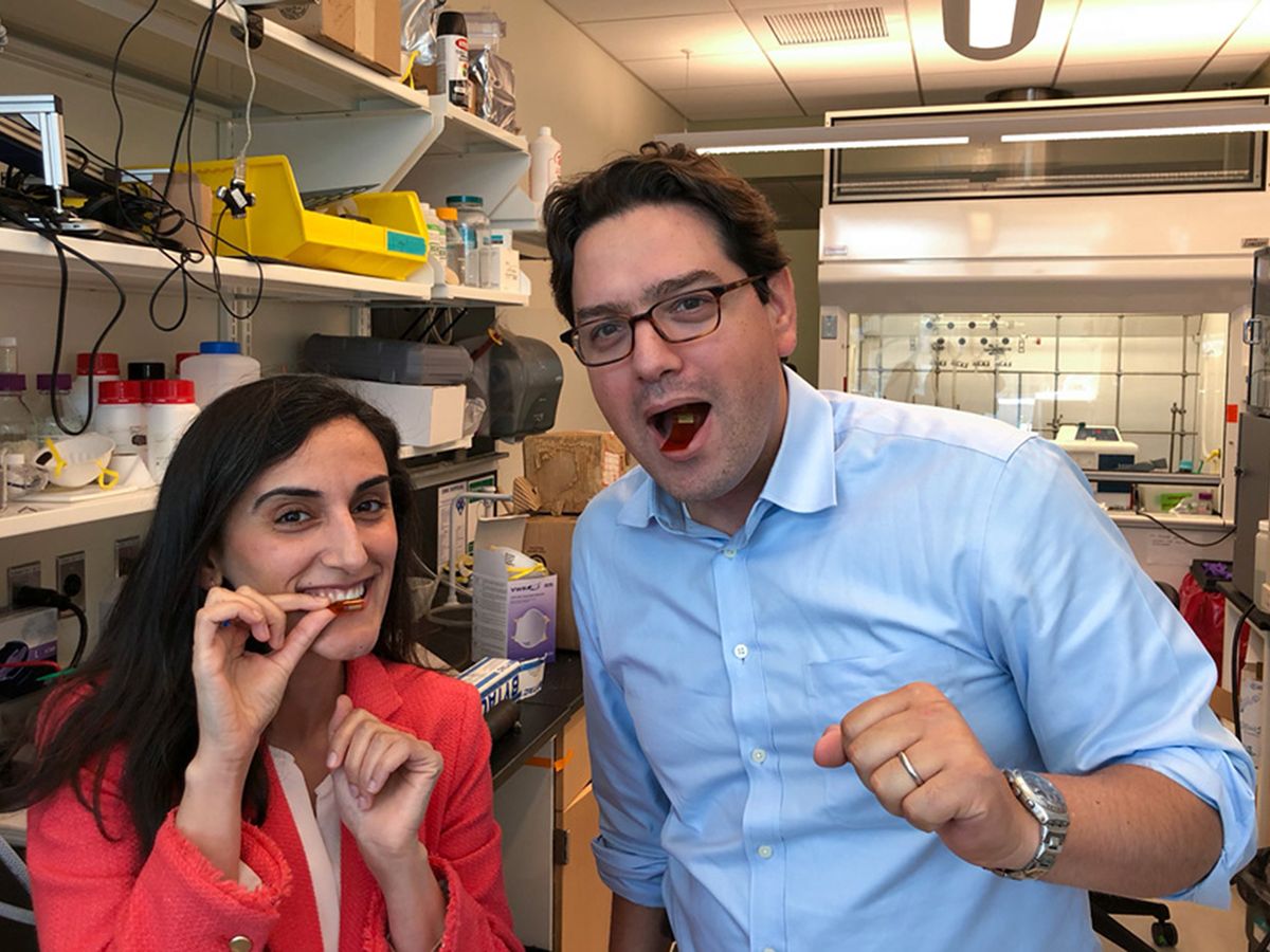 Researchers Canan Dagdeviren and Giovanni Traverso demonstrate their flexible, ingestible device by placing it in their mouths and posing for a photo in a lab. 