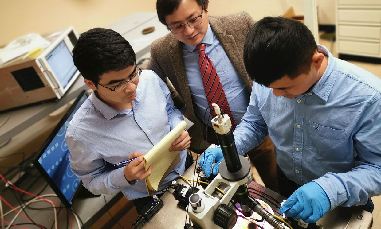 Researchers (from left) Houqiang Fu, Yuji Zhao, Kai Fu work on the memory device at a probe station.