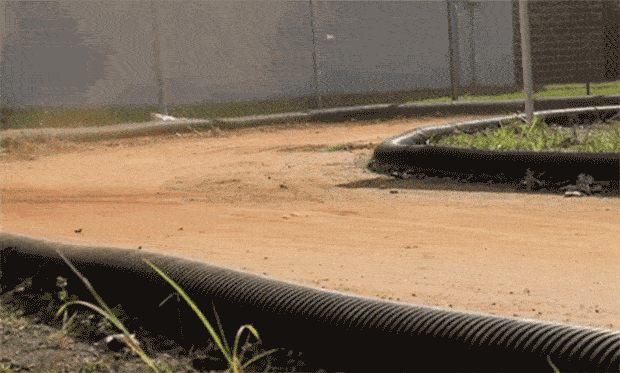 Robotic miniature race car power slides into a turn on a dirt track.
