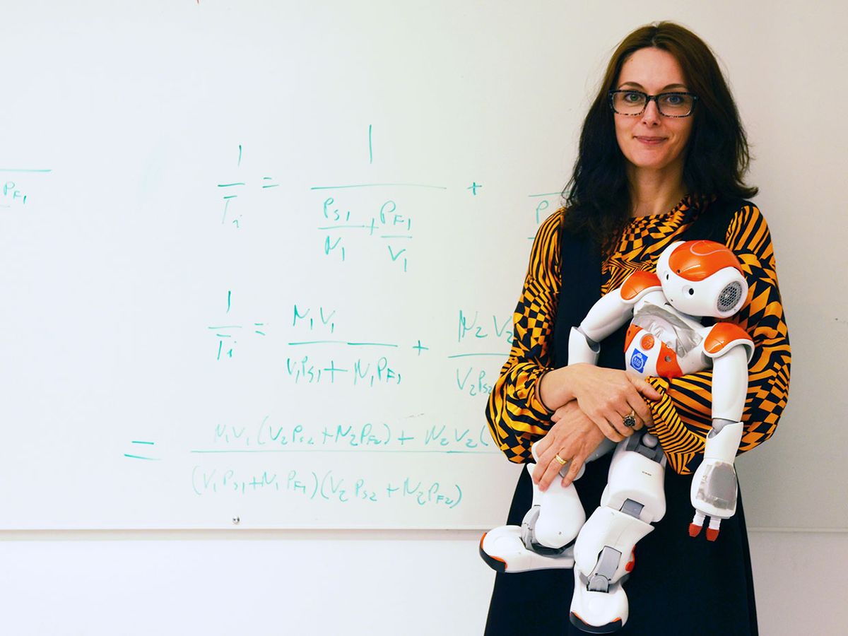 Roboticist Danica Kragic holding a Nao robot in front of a white board with equations on it.