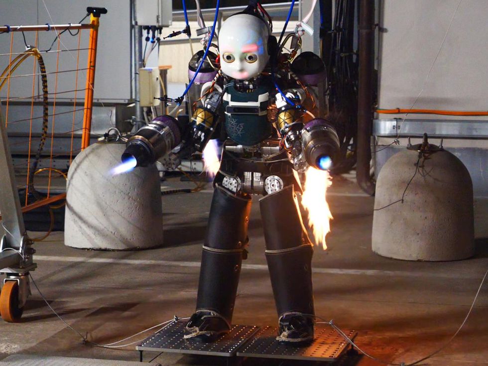 same humanoid robot as in above image but this time in indoor setting with four jet engines on and spewing flames