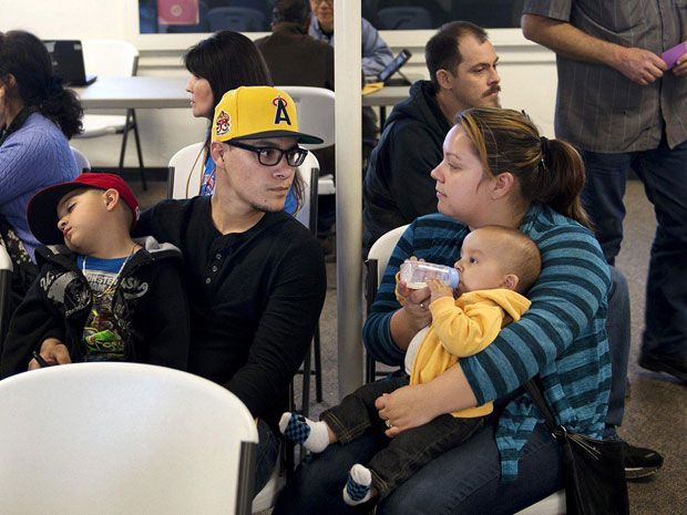 A man and a woman, each with a child in their lap, sit and wait in a crowded room.