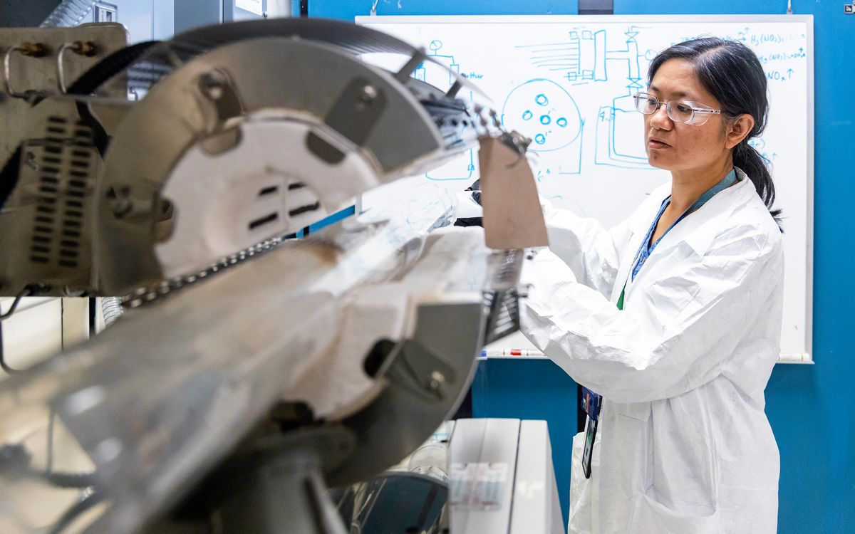 Scientist in lab coat operates machine before a whiteboard with diagrams.