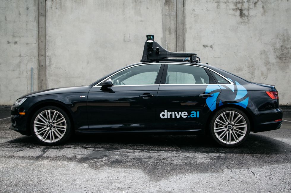 side view of a black car in front of a concrete wall with the words drive ai written on the rear door