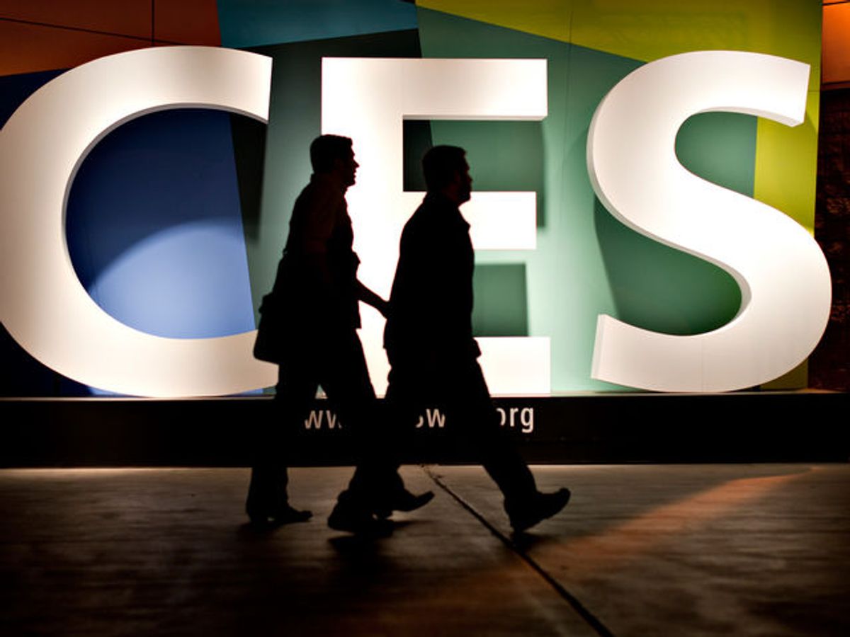 Silhouetted people walk in front of a large logo that spells out CES