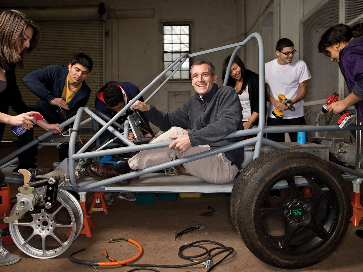 Simon Hauger sits in the frame of a car his students are in the process of building