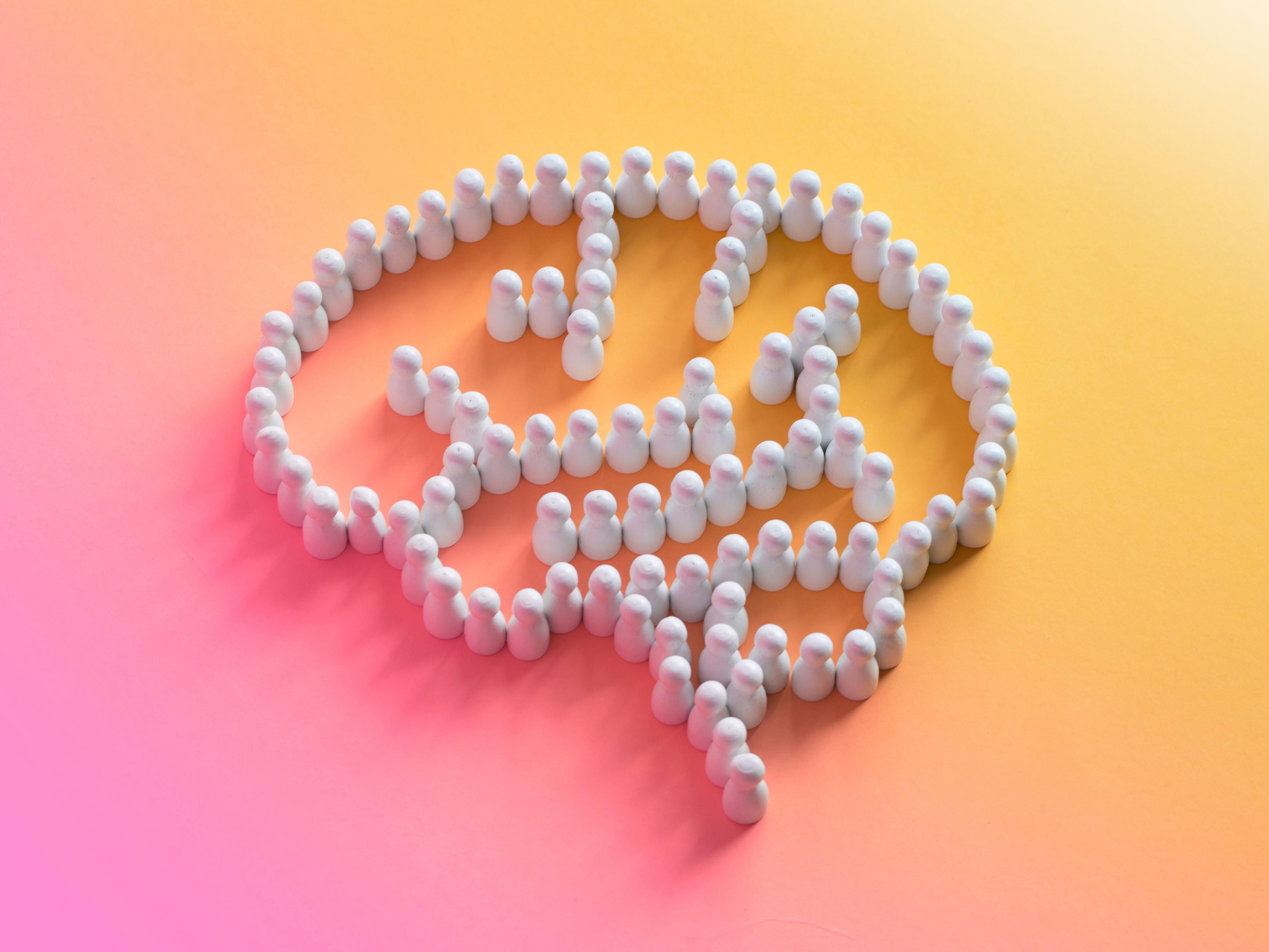 Small white figures collectively form a brain shape on a pink and orange background.