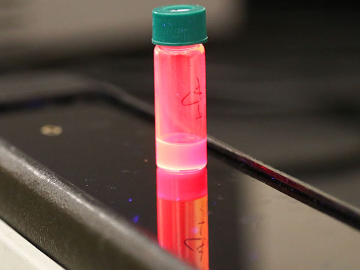 Solution of quantum dots glows bright red when in absorbs light from a UV lamp underneath.
