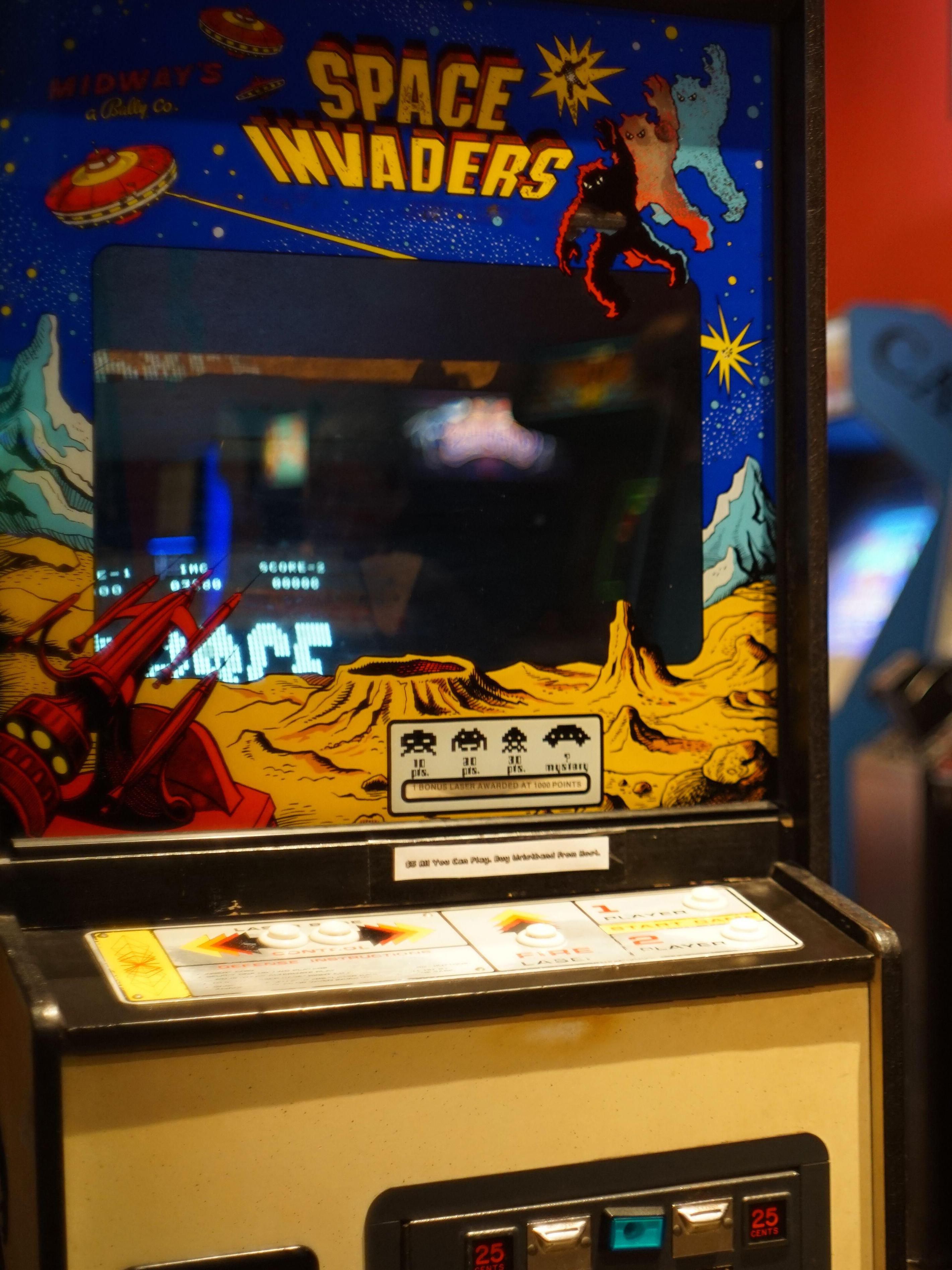 space invaders game in yellow cabinet with black and white screen, other arcade games blurred in background