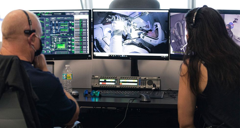 SpaceX employees in front of monitors showing astronauts in Dragon