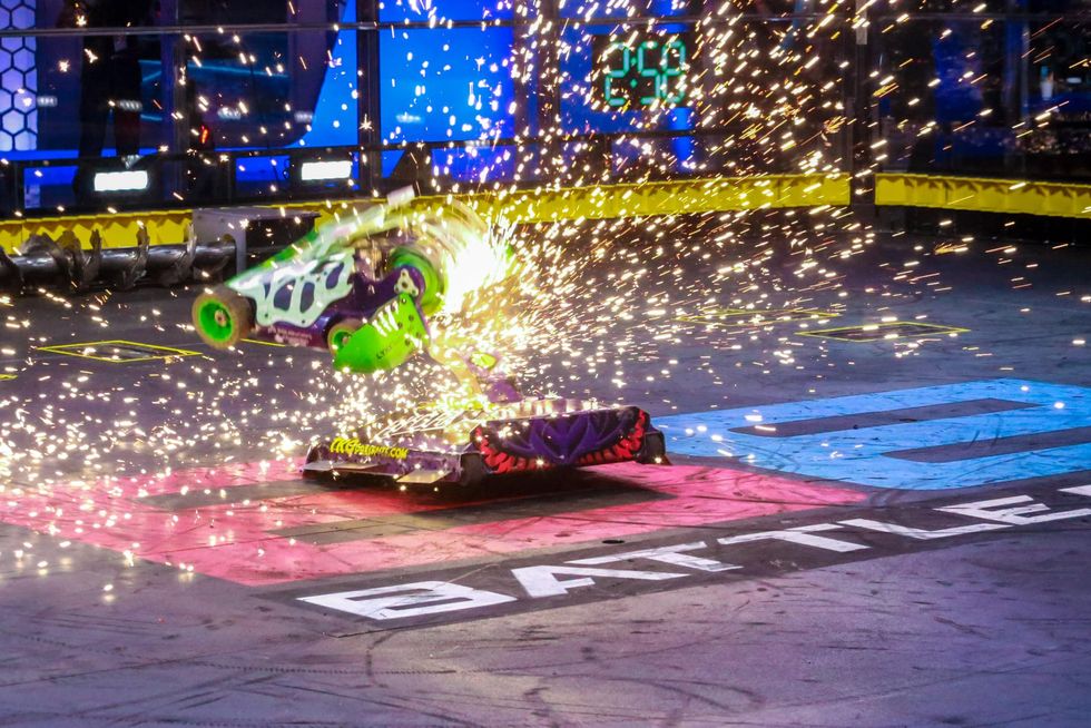 Sparks fly in the BattleBots arena as a green robot attempts to saw open its red-and-black opponent like a can of tuna.