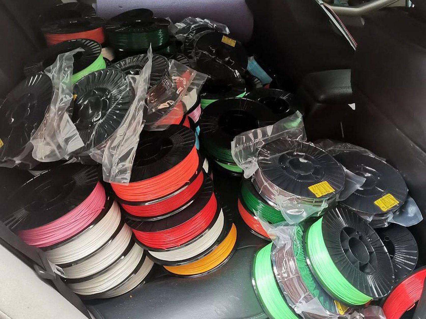 Stacks of colorful spools of 3d printing filament in the back of a car.