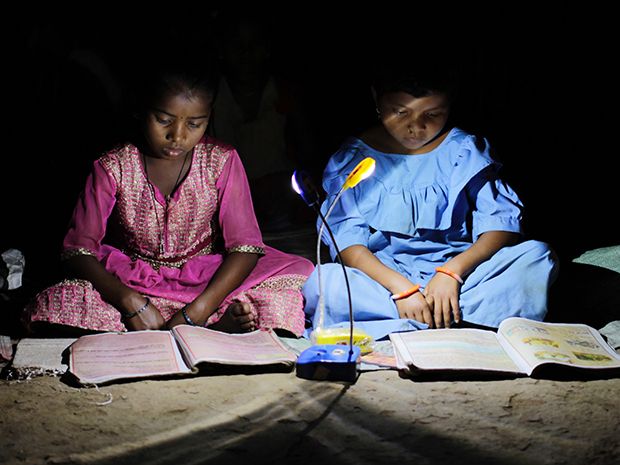 Two girls sit reading school books by LED light.