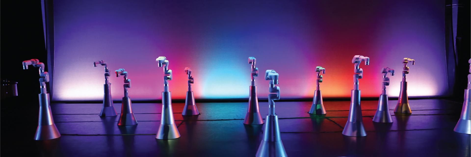 Ten colorfully lit robot arms on metal pedestals spread out across a dance stage