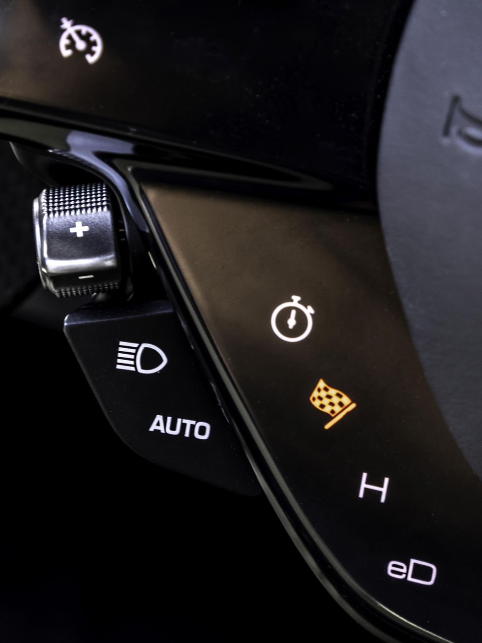 The black inner ring of the steering wheel contains four icons\u2014a white clock face, a yellow checkered flag, a white letter \u201cH,\u201d and the white letters \u201ceD.\u201d 