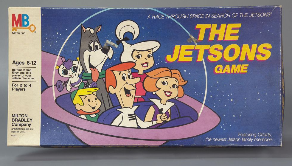 The cardboard cover of a board game called \u201cThe Jetsons Game\u201d shows a cartoon family of four plus two pets in a spacecraft.