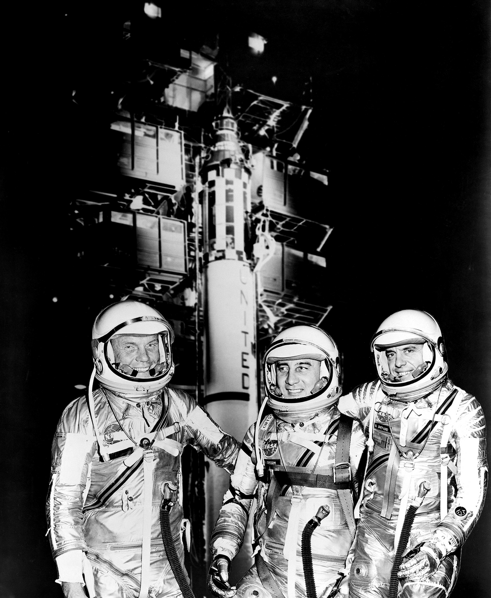 The image shows a Redstone rocket at the launch pad, with three space-suit-wearing astronauts in the foreground.