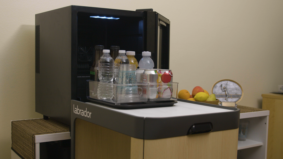 The Labrador robot is shown in front of a fridge with the door open, retrieving food on a tray.