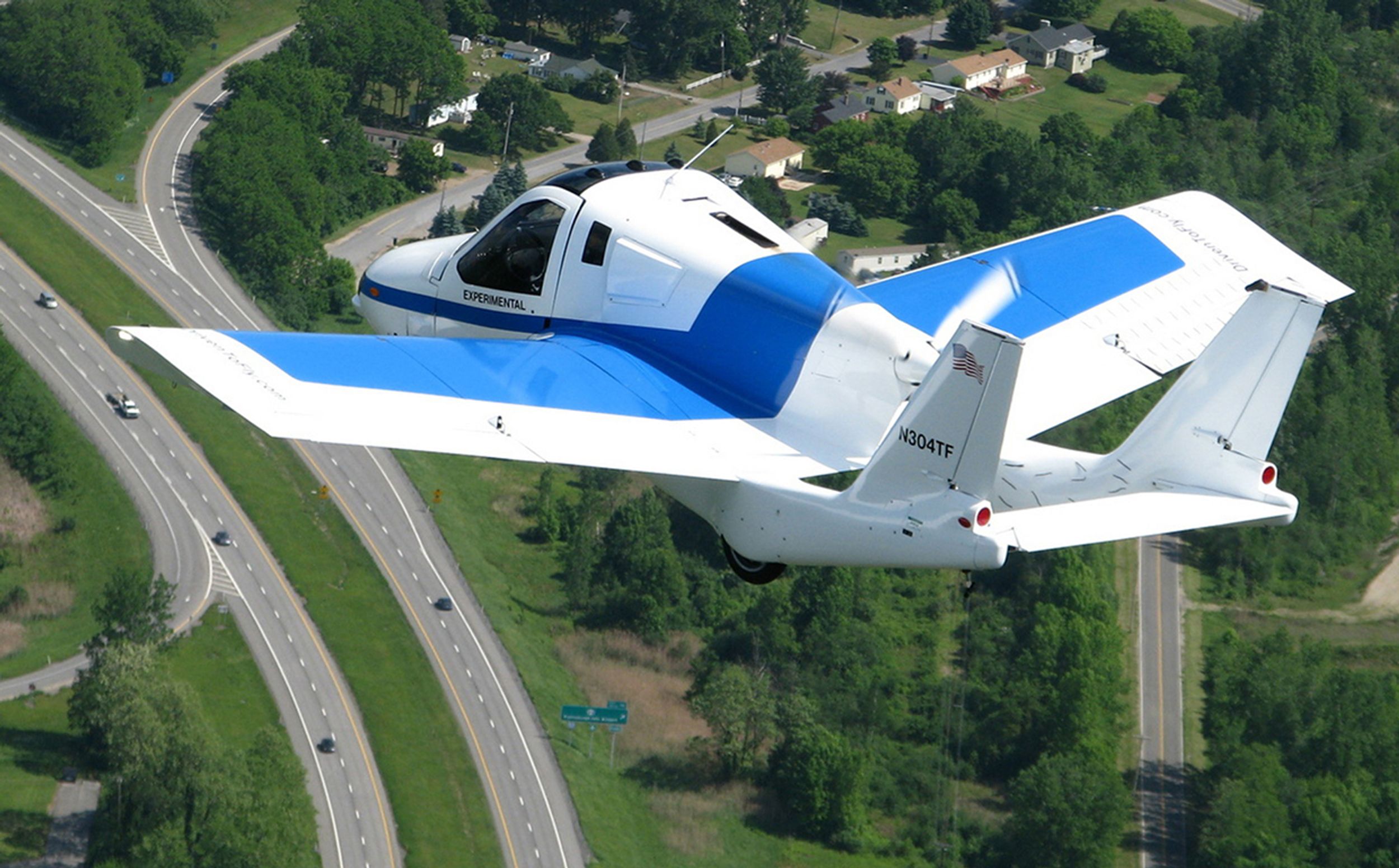 The Terrafugia flying car is seen in the air, with roads below.