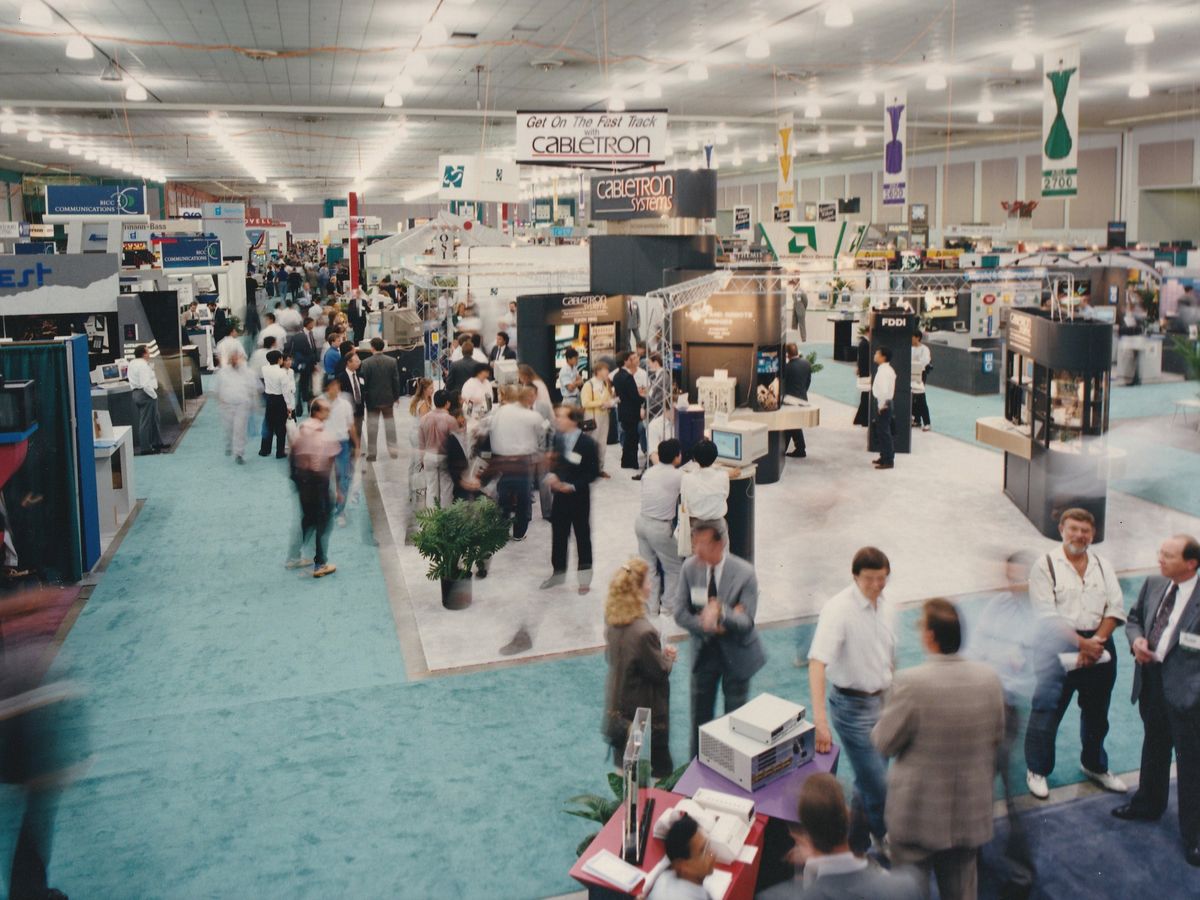 This photograph of the exhibition floor shows a large number of people moving about and visiting booths set up by IBM and Sony, among many other companies.   