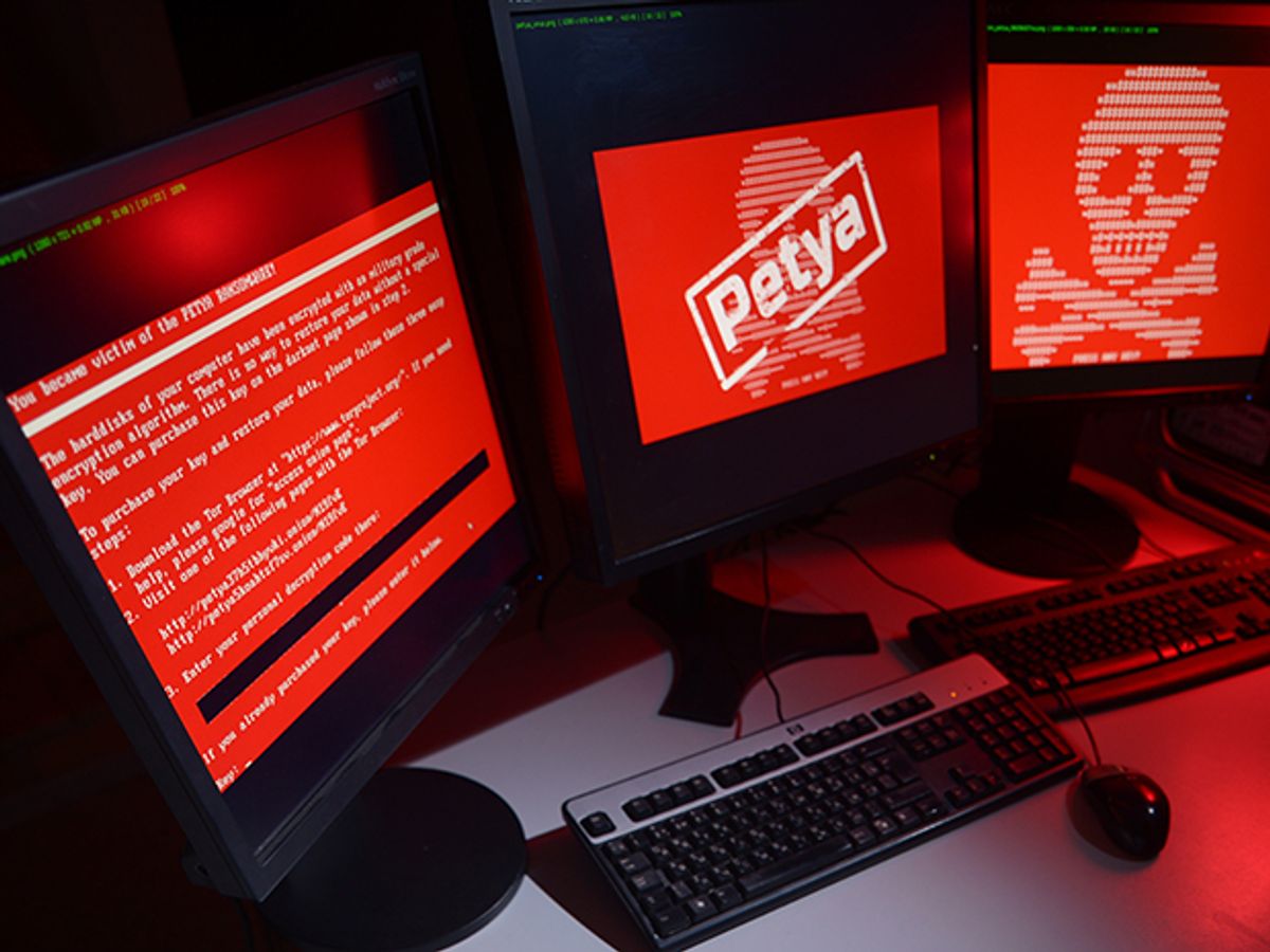 Three computer screens glow red, showing computer code and a skull and cross bones in white text