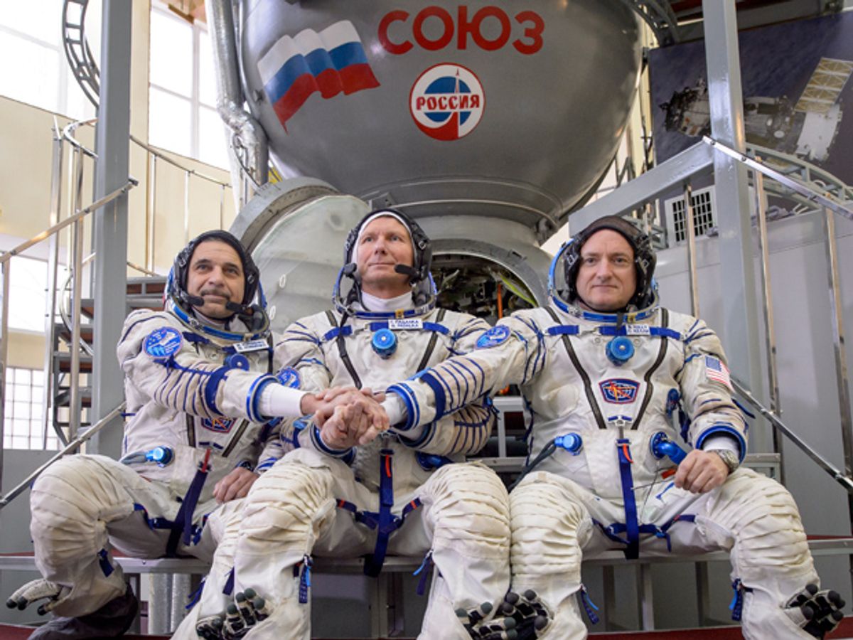 Three men sit in space suits in front of a metal capsule