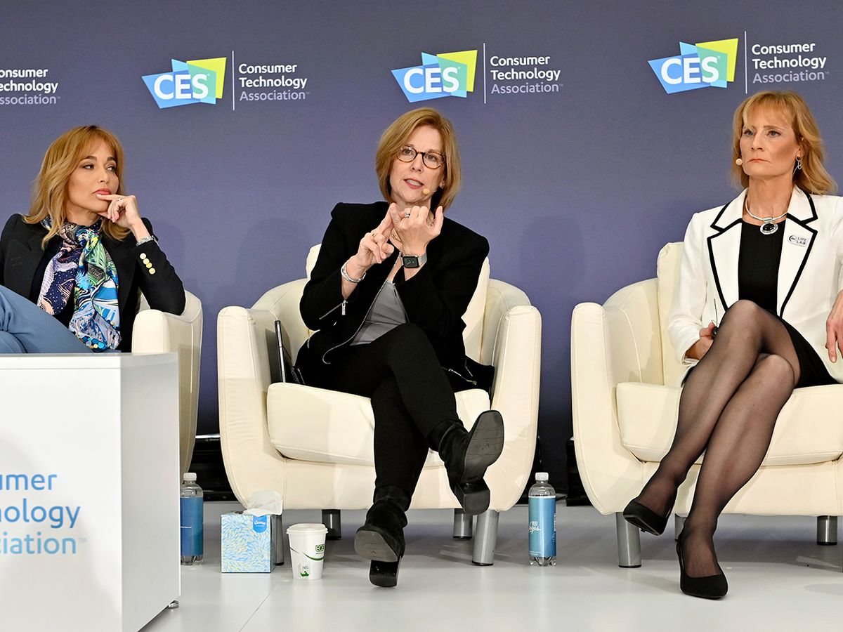 Three panelists sit in white chairs on a stage in front of a colorful backdrop that says CES.