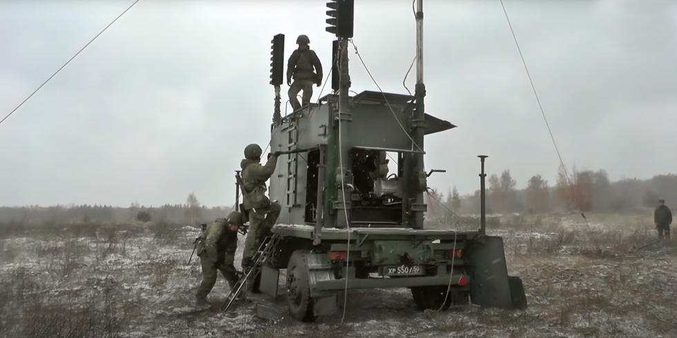 Three Russian soldiers climb on a wheeled vehicle supporting an antenna.