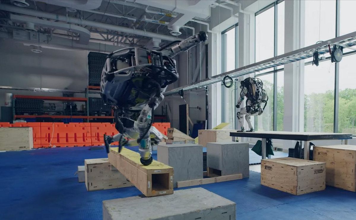 Two bulky humanoid robots clamber over an indoor obstacle course