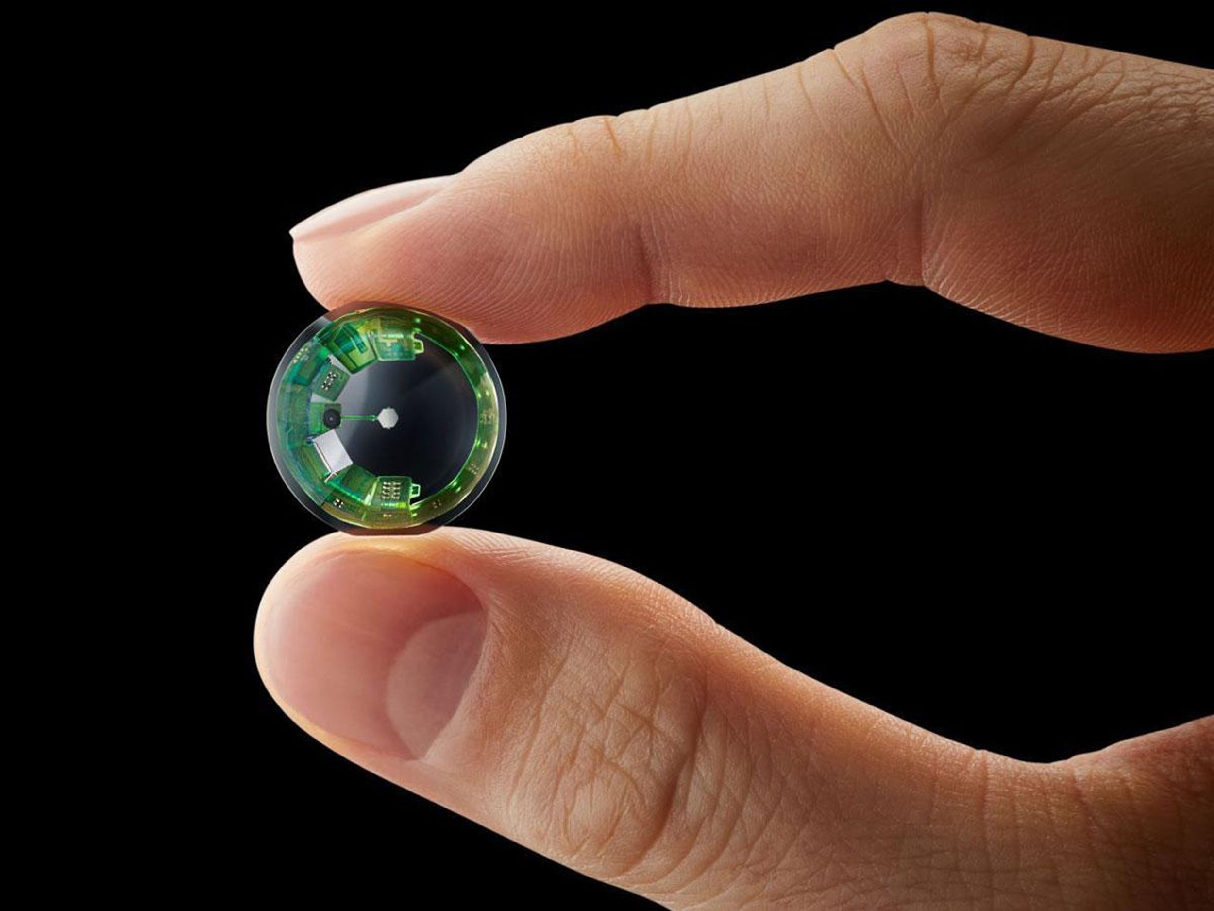 Two fingers hold a contact lens with a ring of circuitry on its outer edge