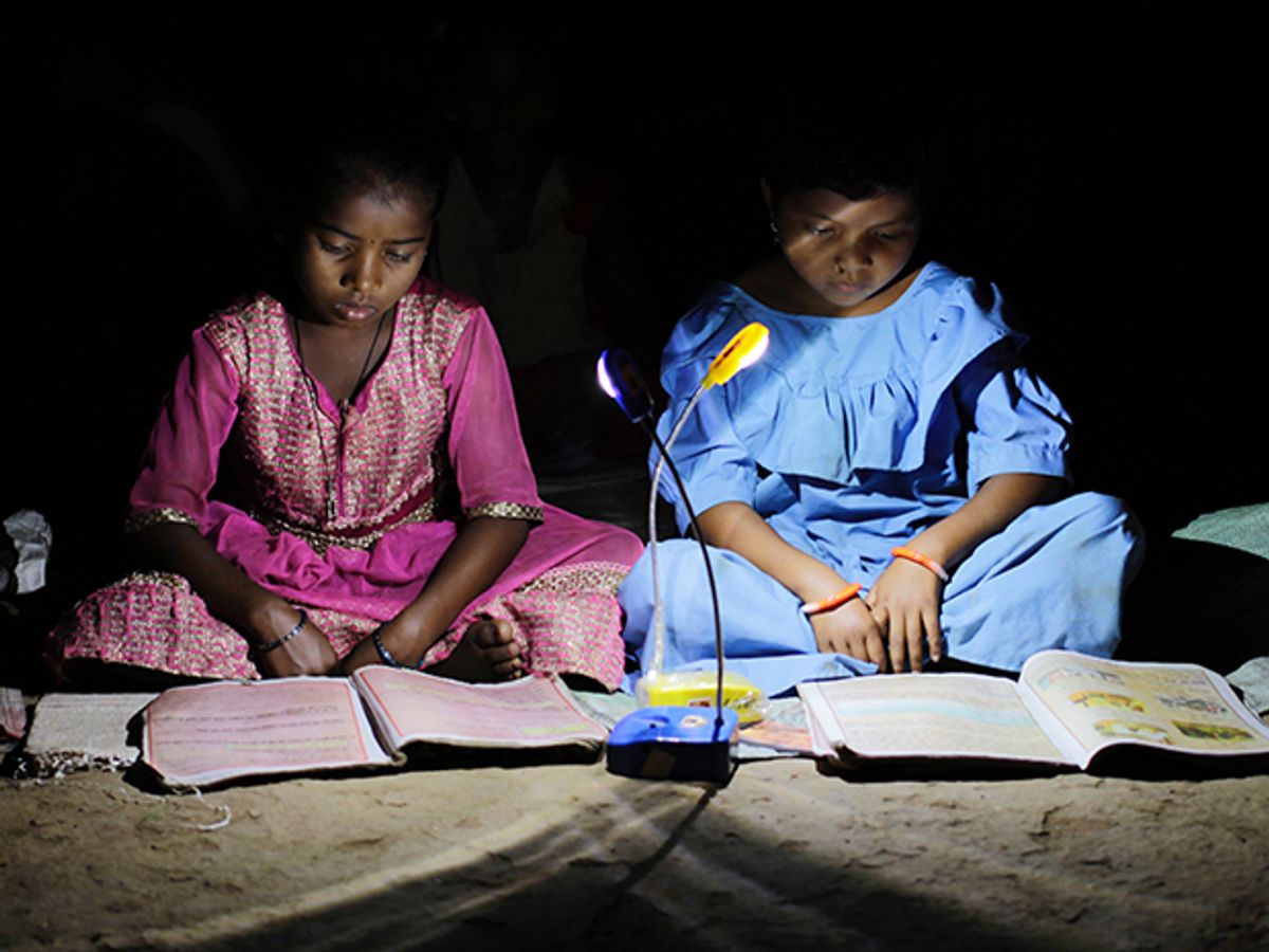 Two girls sit reading school books by LED light.
