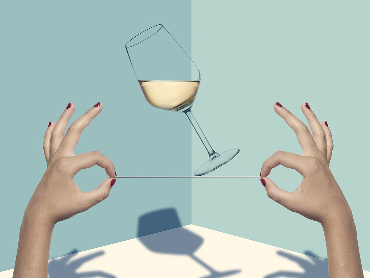 Two hands hold a string tightrope for a tipping glass of wine.