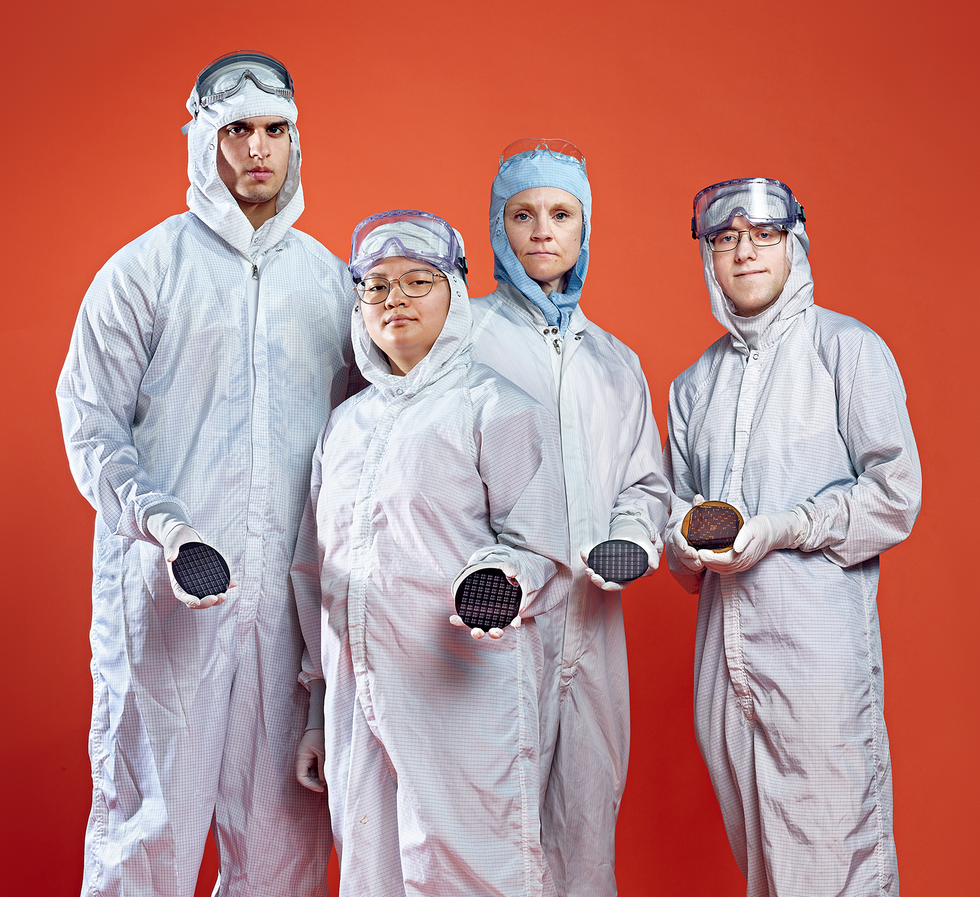 Two men and two women, all dressed in white jump suits with hoods stand in front of an orange background. Each holds a palm-sized black disc. 