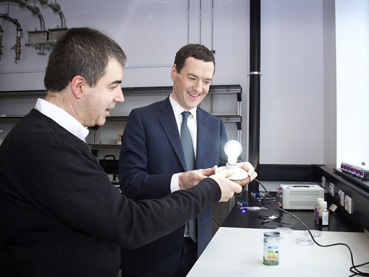Two men in a laboratory gaze at an illuminated lightbulb mounted in a fixture they are holding in their hands