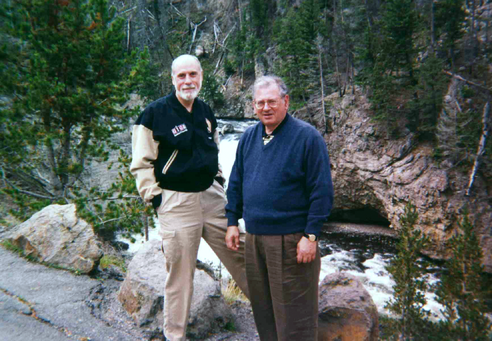 Two men in casual dress stand in front of a rocky trail