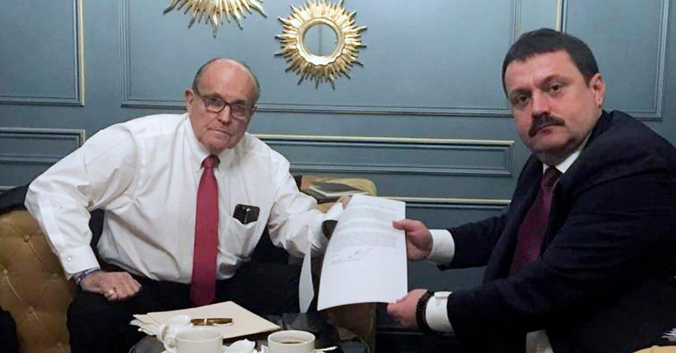 Two men in suits show a document that they hold together
