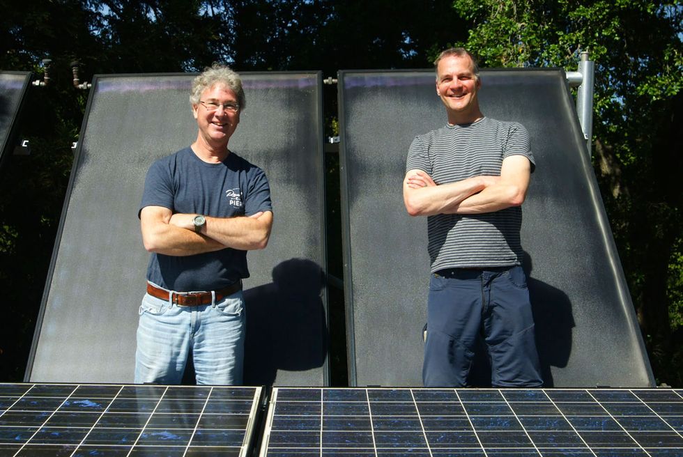 Two men standing in front of a solar panel. 