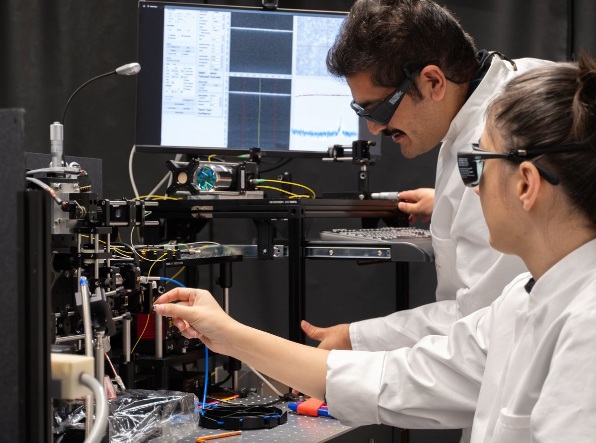 Two people in laboratory glasses adjust a laser system on a table