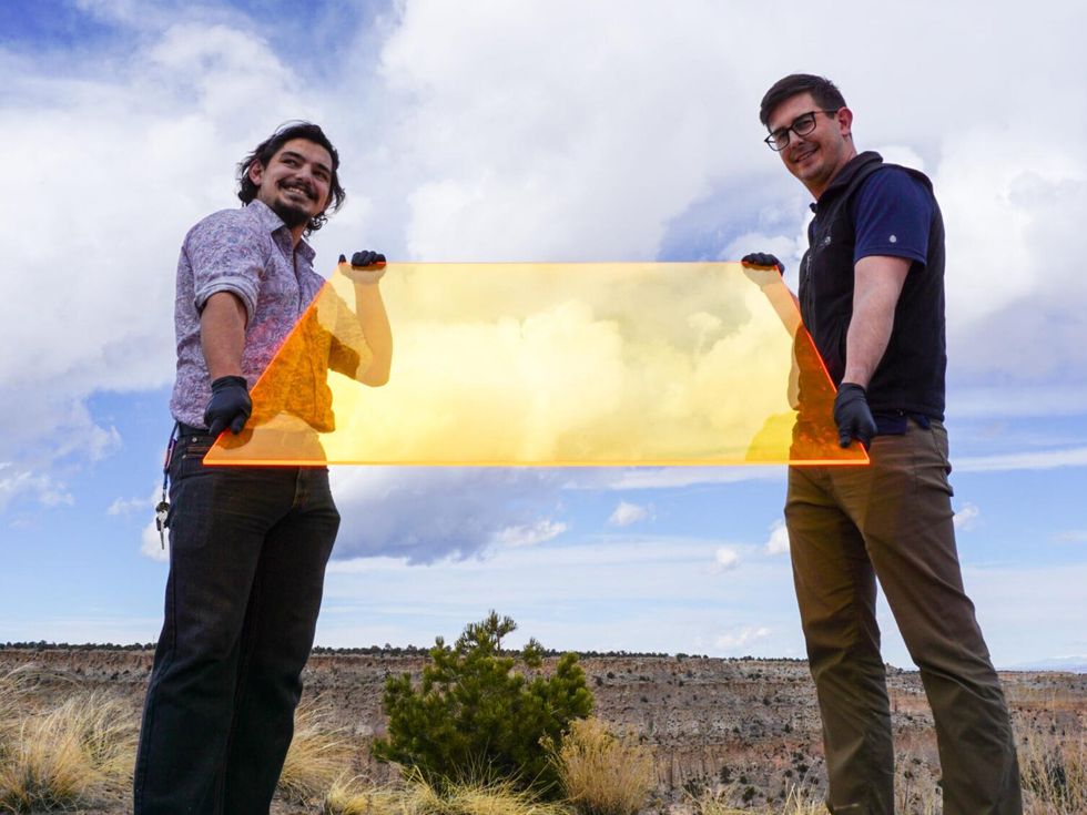 Two people stand in a field holding a large translucent yellow rectangle.