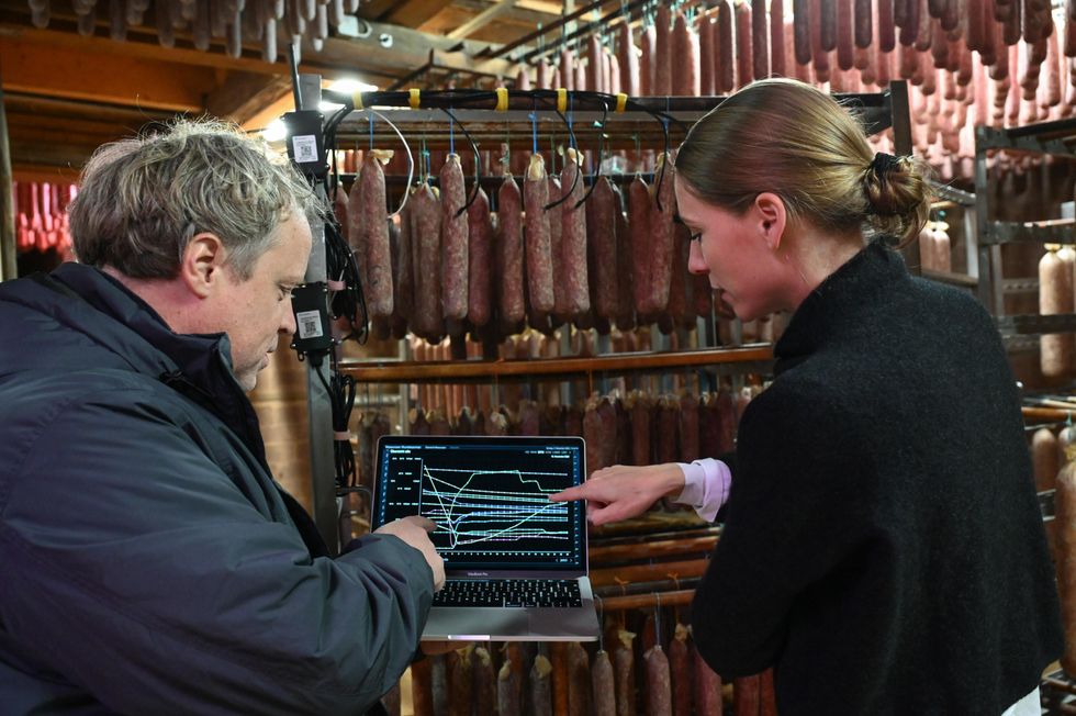 Two people standing in a room of sausages pointing to a small laptop.