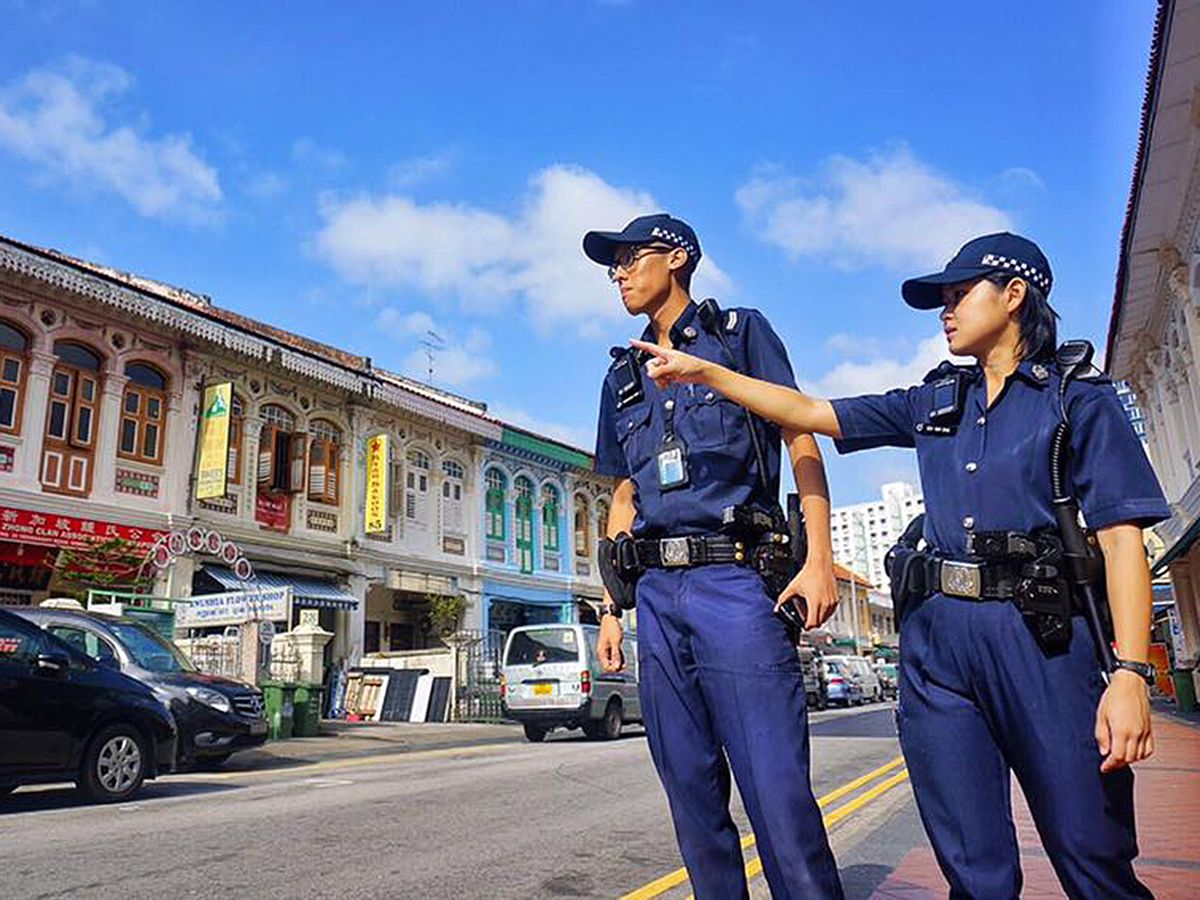 Two police officers dressed in uniform stand to the side of a street in Singapore.