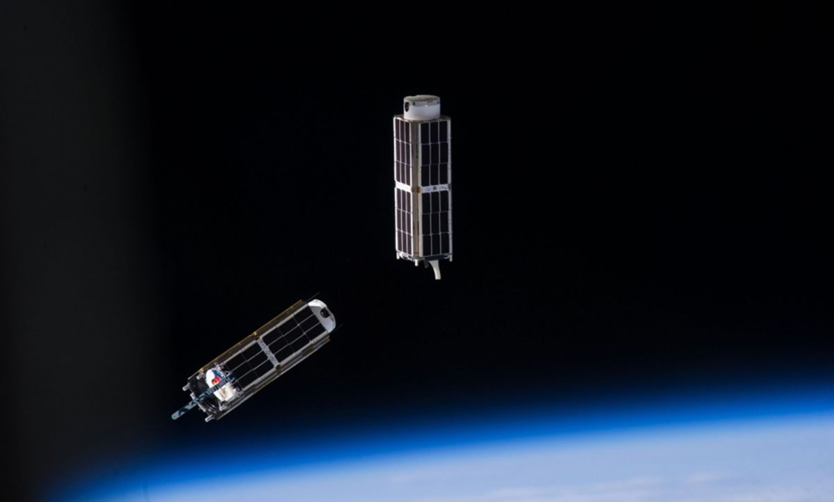 Two rectangular objects covered with black solar cells in orbit above the Earth