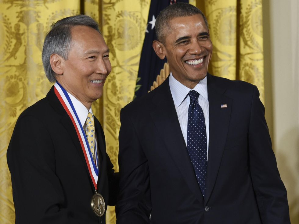 Two smiling men in suits. The man on the left wears a large golden medal around his neck.
