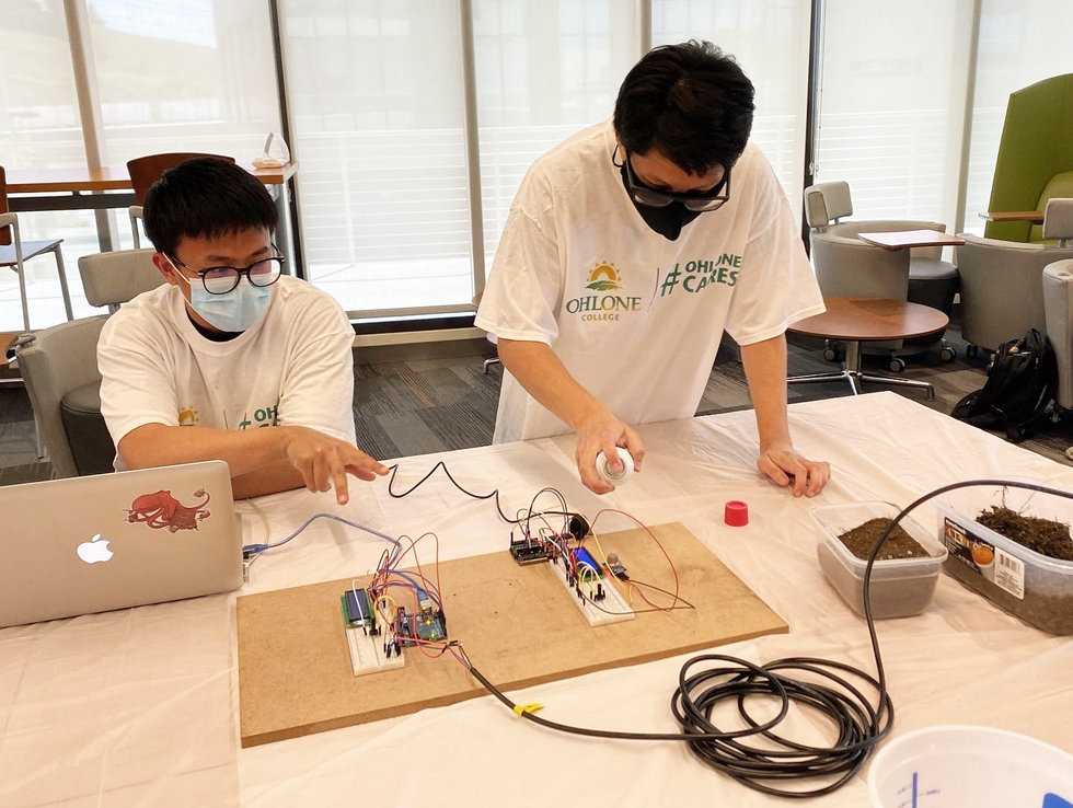 Two young men are in front of two sensor systems wired to a piece of wood.