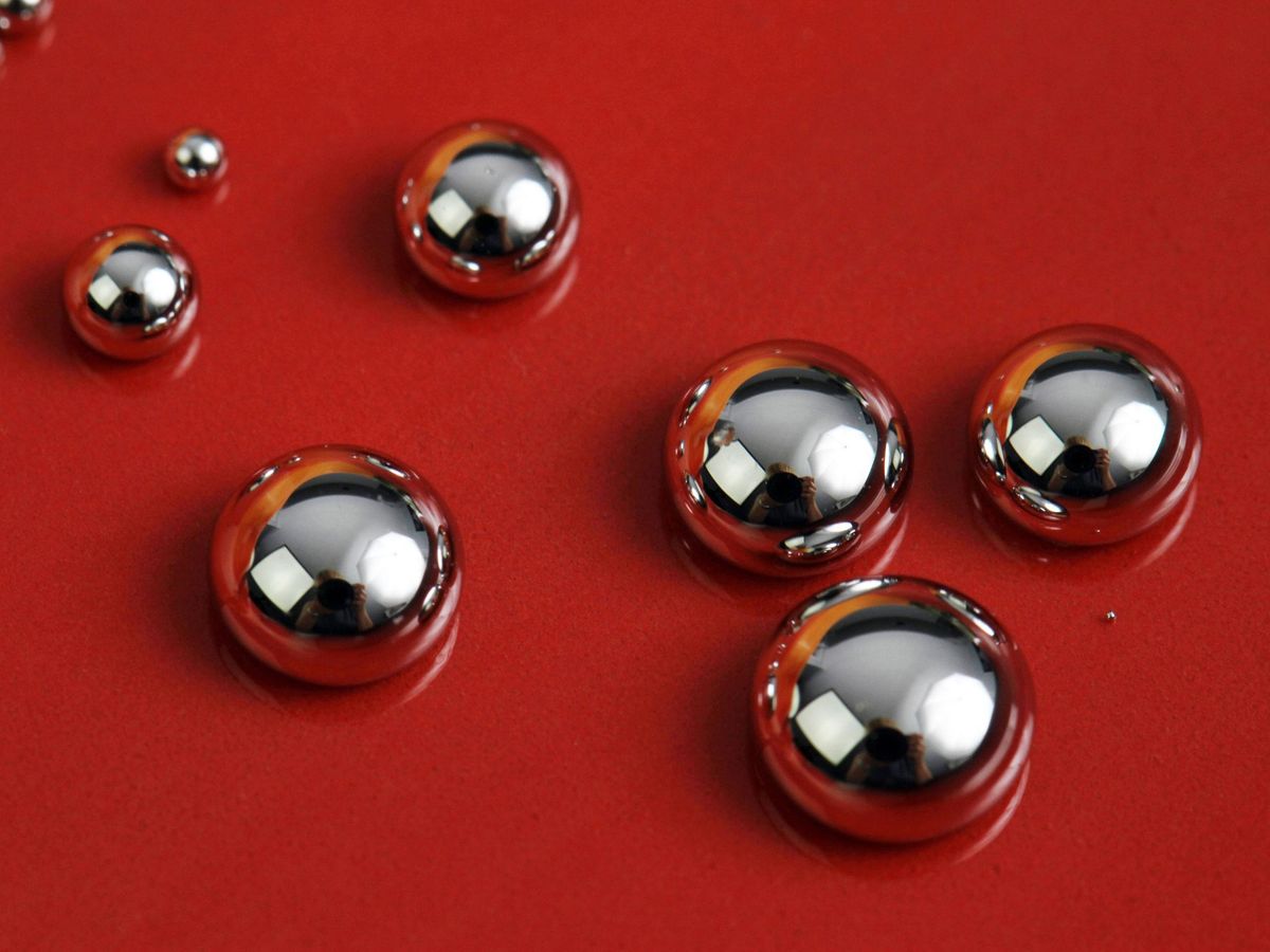 Variously sized drops of a silver liquid metal beading up on a red background.